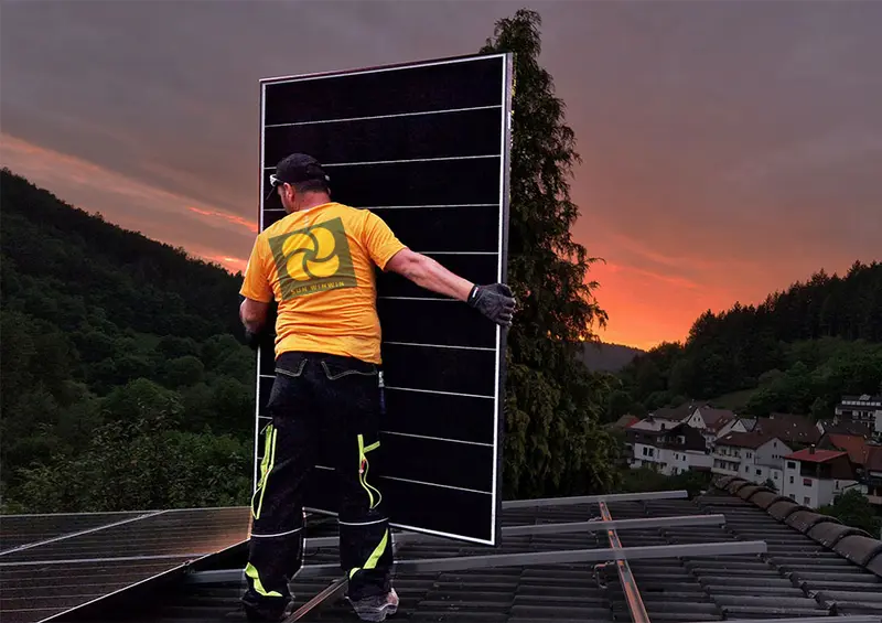 Monteur mit Solarmodul auf einem Steildach